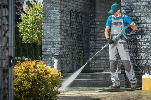 Driveway Pressure Washing. Caucasian Worker Cleaning Area in Front of the House.